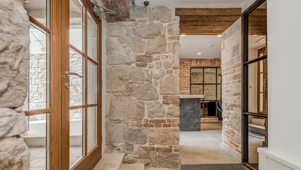 A stone-walled hallway leading to a fireplace, with a wooden door and a view of a room with a fireplace. - Stonemasons Heritage (Split)