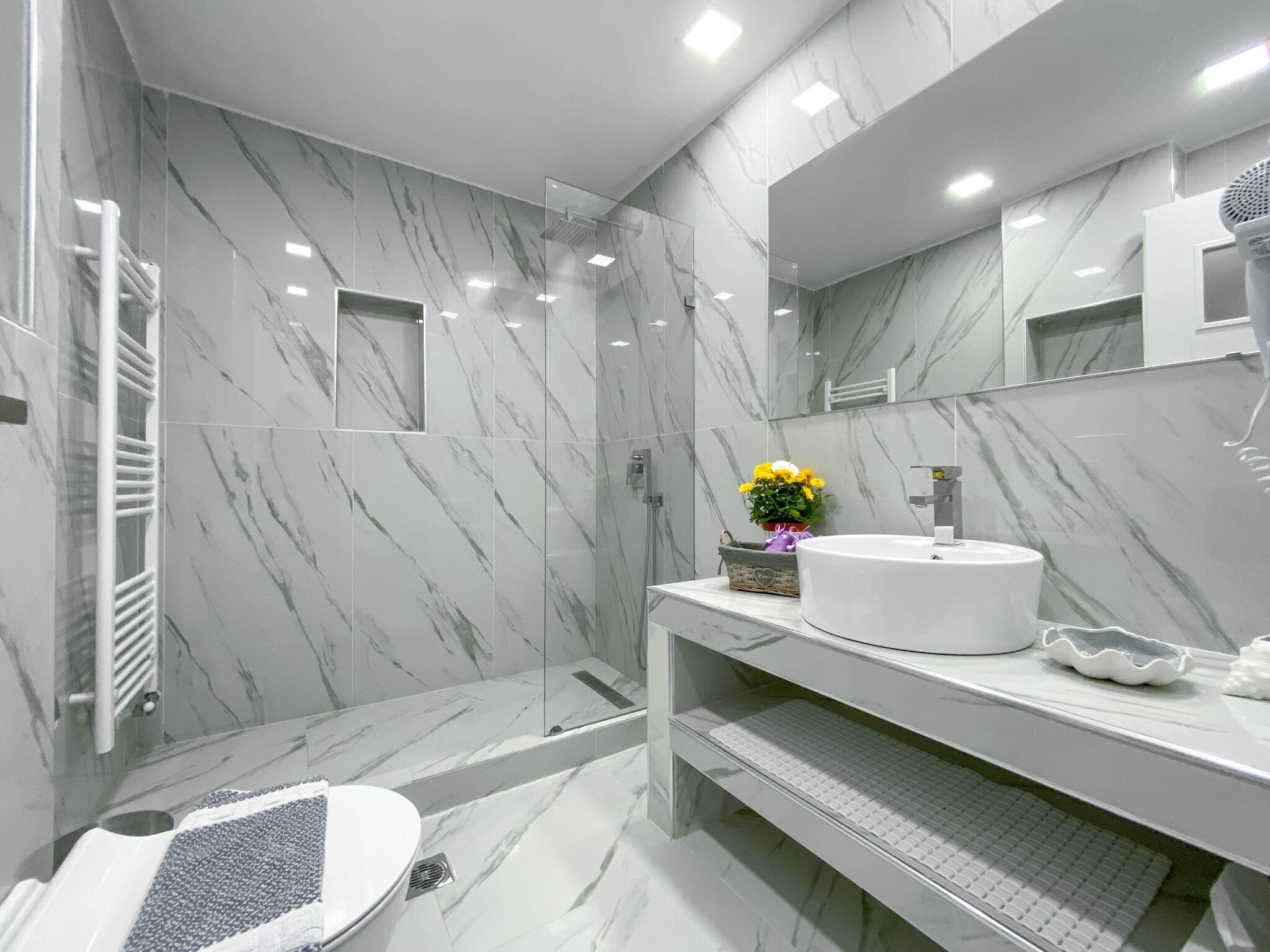 A modern bathroom with a marble backsplash, a large mirror, and a white sink.