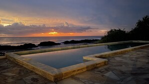Una piscina infinita con vista al océano y al atardecer.