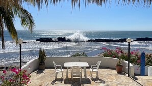 Un patio con mesa y sillas con vista al océano, cubierto por un techo de paja.