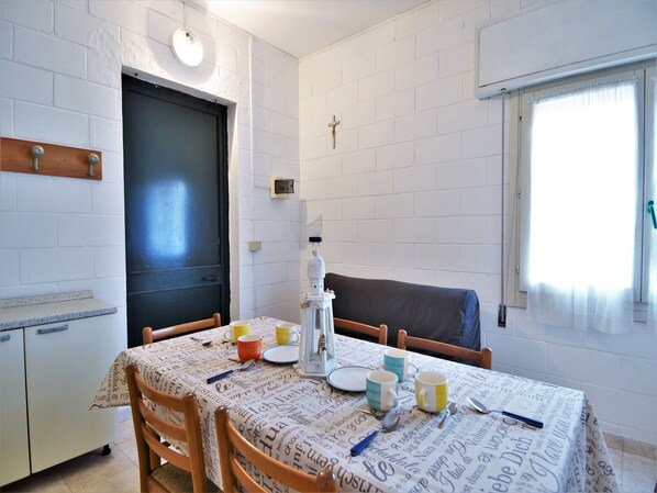 A dining area with a table set for four, featuring a tablecloth with printed text, four chairs, a water dispenser, and a cross on the wall.