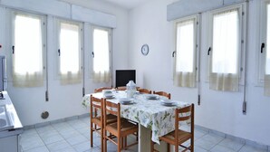 A dining area with a table set for four, a clock on the wall, and windows with curtains. - Coastal Comfort in Rosolina (Rosolina Mare (RO))