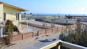 A coastal hotel with a yellow building, a fenced tennis court, and a view of the sea. - Coastal Comfort in Rosolina (Rosolina Mare (RO))