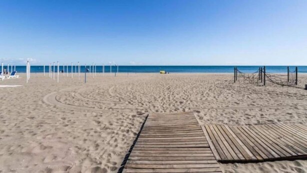 A beach with a wooden boardwalk leading to the water, a clear sky, and a distant yellow vehicle. - Coastal Comfort in Rosolina (Rosolina Mare (RO))