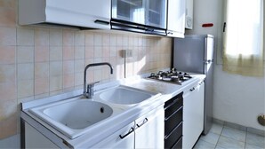 A kitchen with white cabinets, a double sink, a gas stove, and a window with a curtain. - Coastal Comfort in Rosolina (Rosolina Mare (RO))