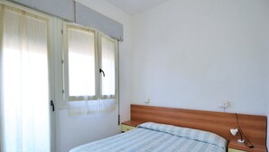 A bedroom with a bed, a wooden headboard, a nightstand with a lamp, and a window with curtains. - Coastal Comfort in Rosolina (Rosolina Mare (RO))