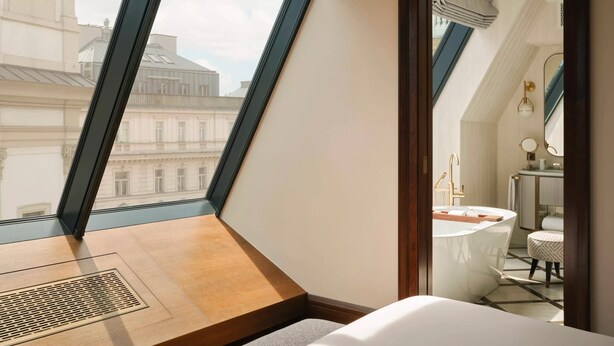 A modern hotel room with a large skylight, a wooden desk, and a view of historic buildings. - Rosewood Vienna (Vienna)