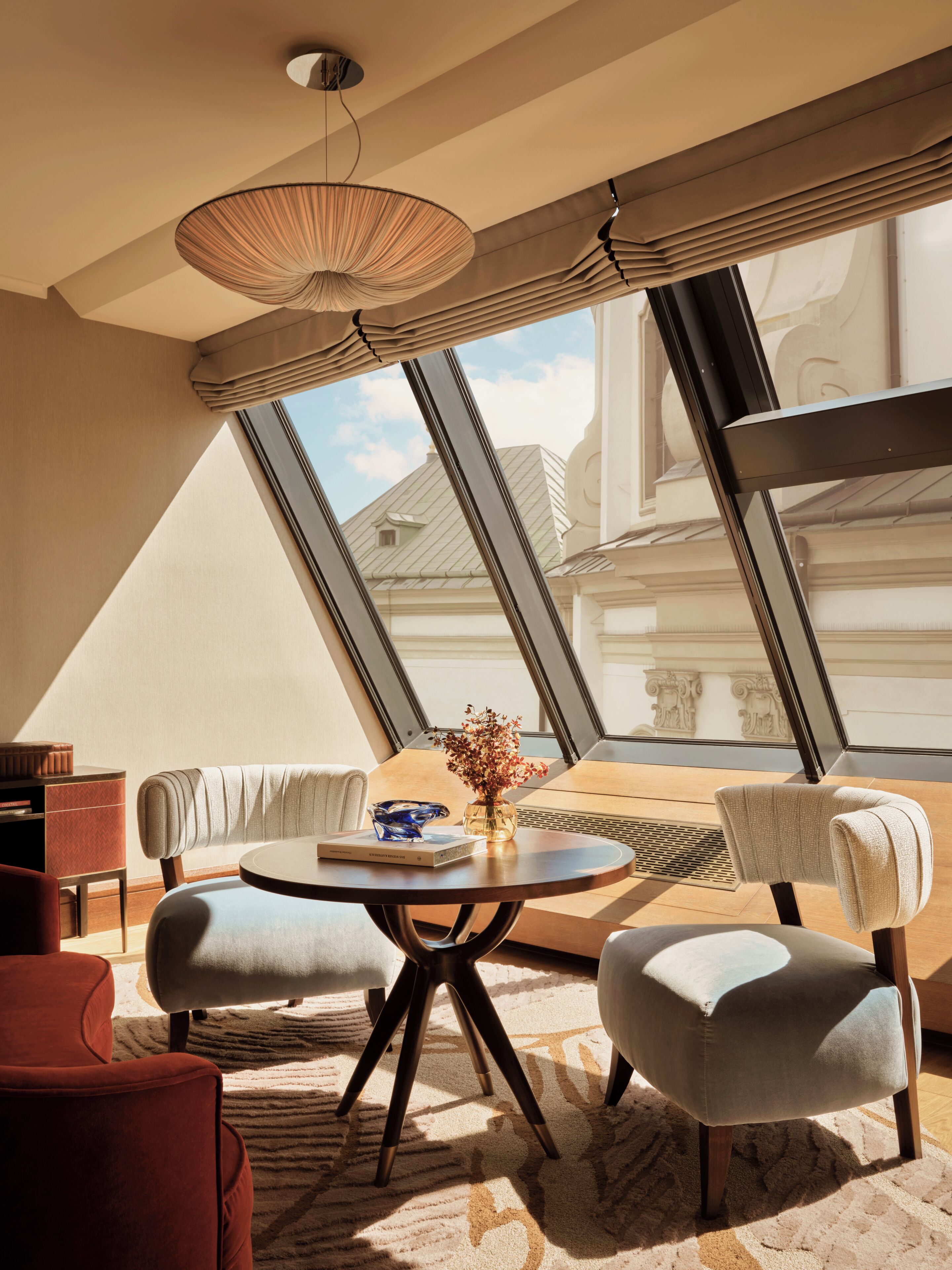 Un interior moderno con una mesa redonda, dos sillones, un sofá y un amplio ventanal con vistas a edificios.