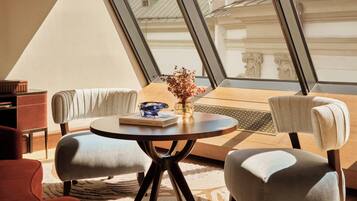 Un interior moderno con una mesa redonda, dos sillones, un sofá y un amplio ventanal con vistas a edificios.