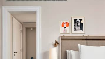 Habitación de hotel con cama, mesita de noche con lámpara, reloj y dos cuadros en la pared.