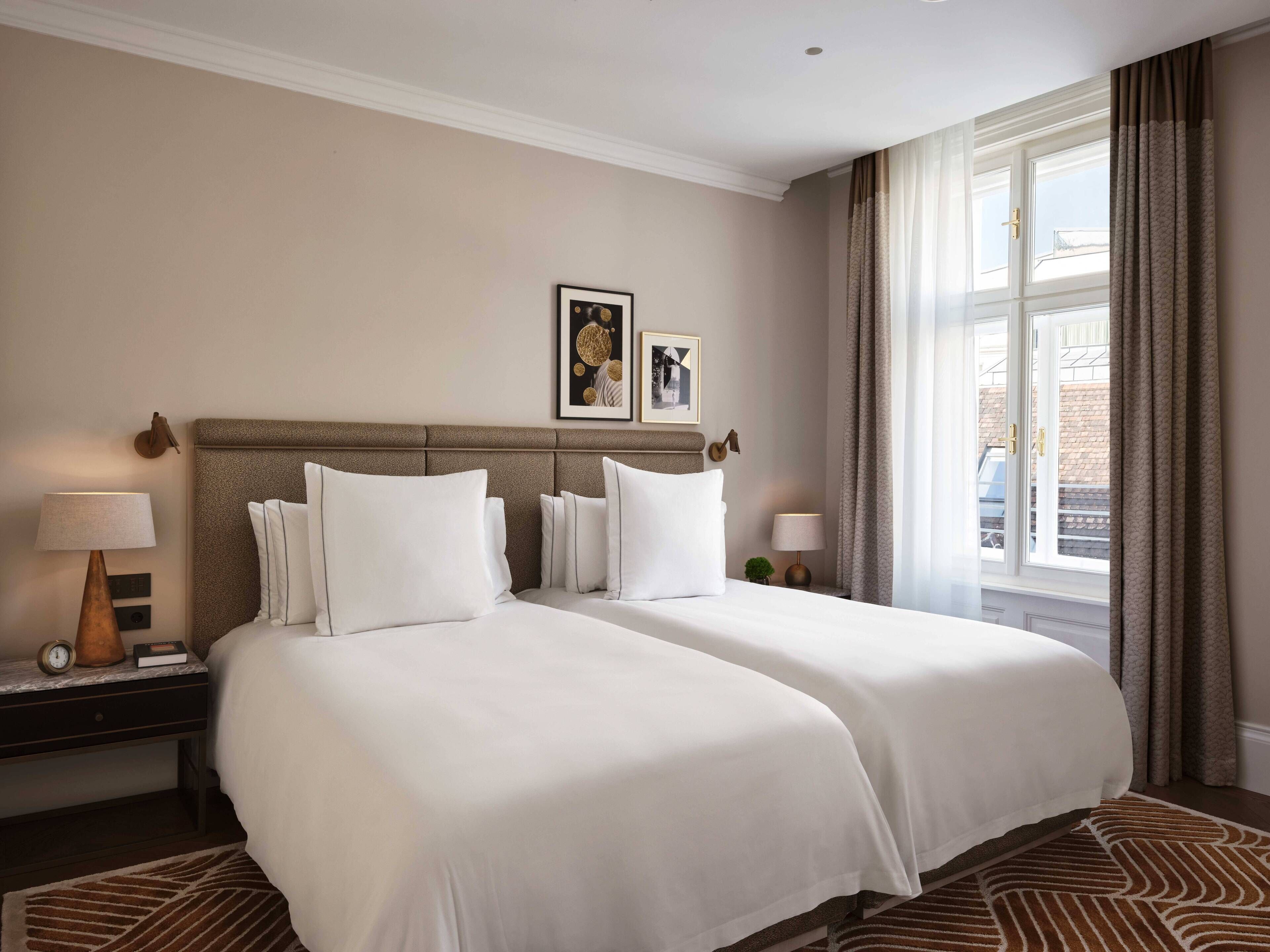 Habitación de hotel con dos camas, una mesita de noche con lámpara, un reloj y un cuadro en la pared.