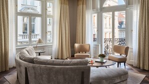 A spacious living room with a curved sofa, two armchairs, a coffee table, and large windows with curtains. - Rosewood Vienna (Vienna)