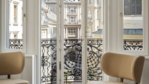 A room with a view of historic buildings, a round table with a vase of flowers, and two chairs. - Rosewood Vienna (Vienna)