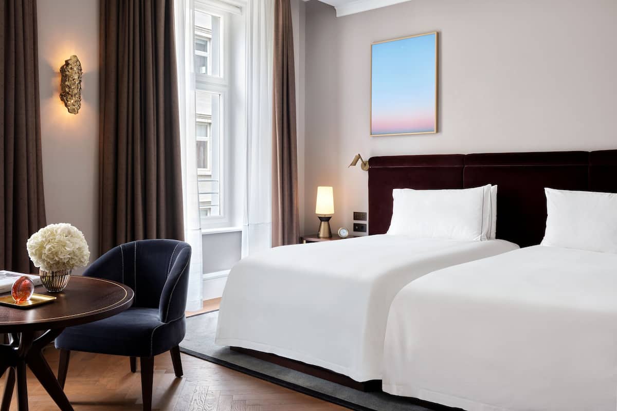 A hotel room with a large bed, a desk with a chair, a vase with flowers, and a painting on the wall.