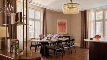 A dining area with a round table, chairs, a chandelier, and a view of the city through large windows.