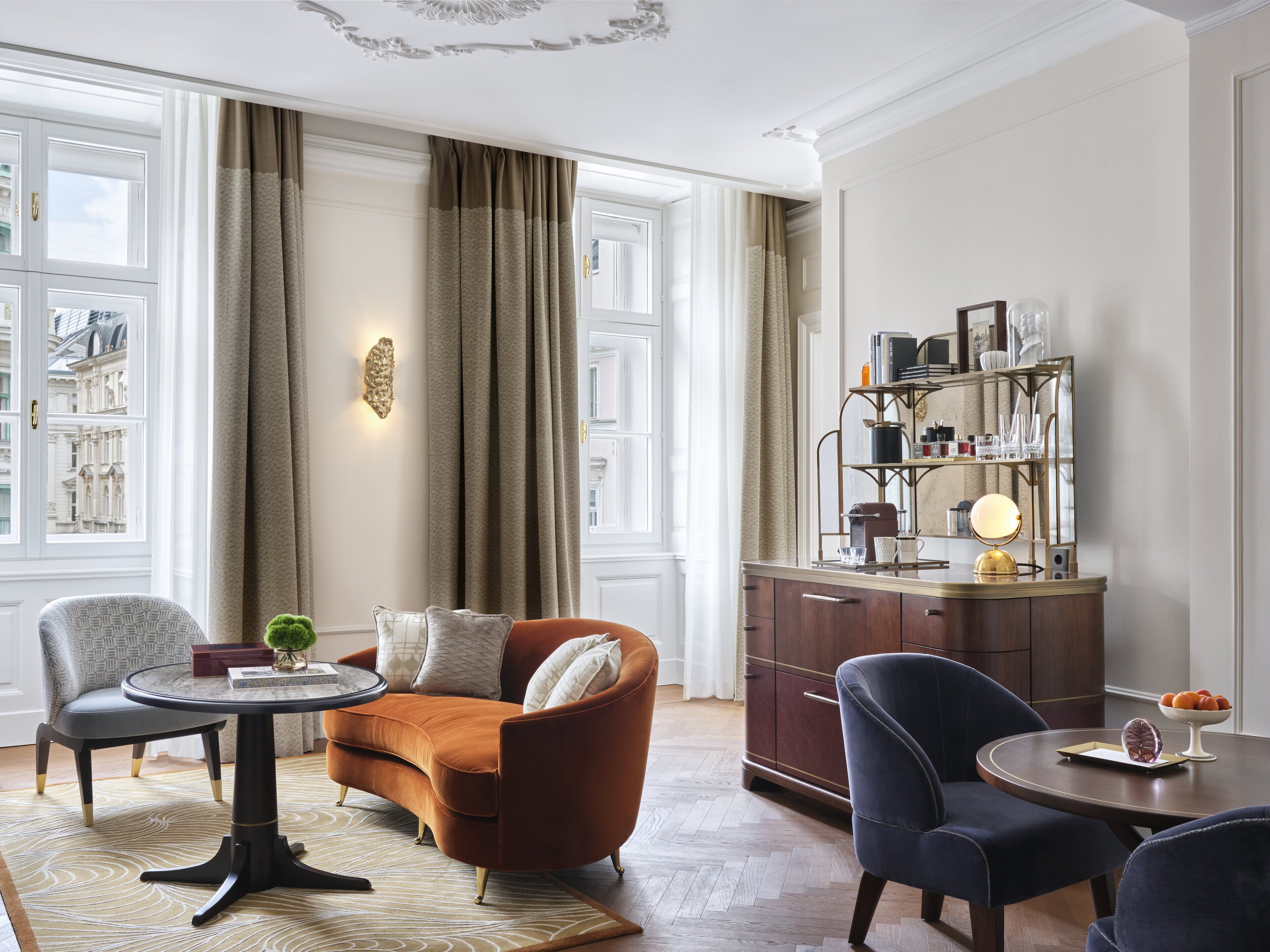 A well-lit living room with a sofa, armchairs, a coffee table, and a sideboard with decorative items.