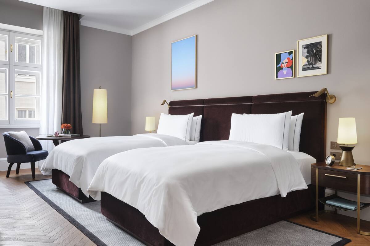 A hotel room with two beds, a desk, a chair, and a window with curtains.