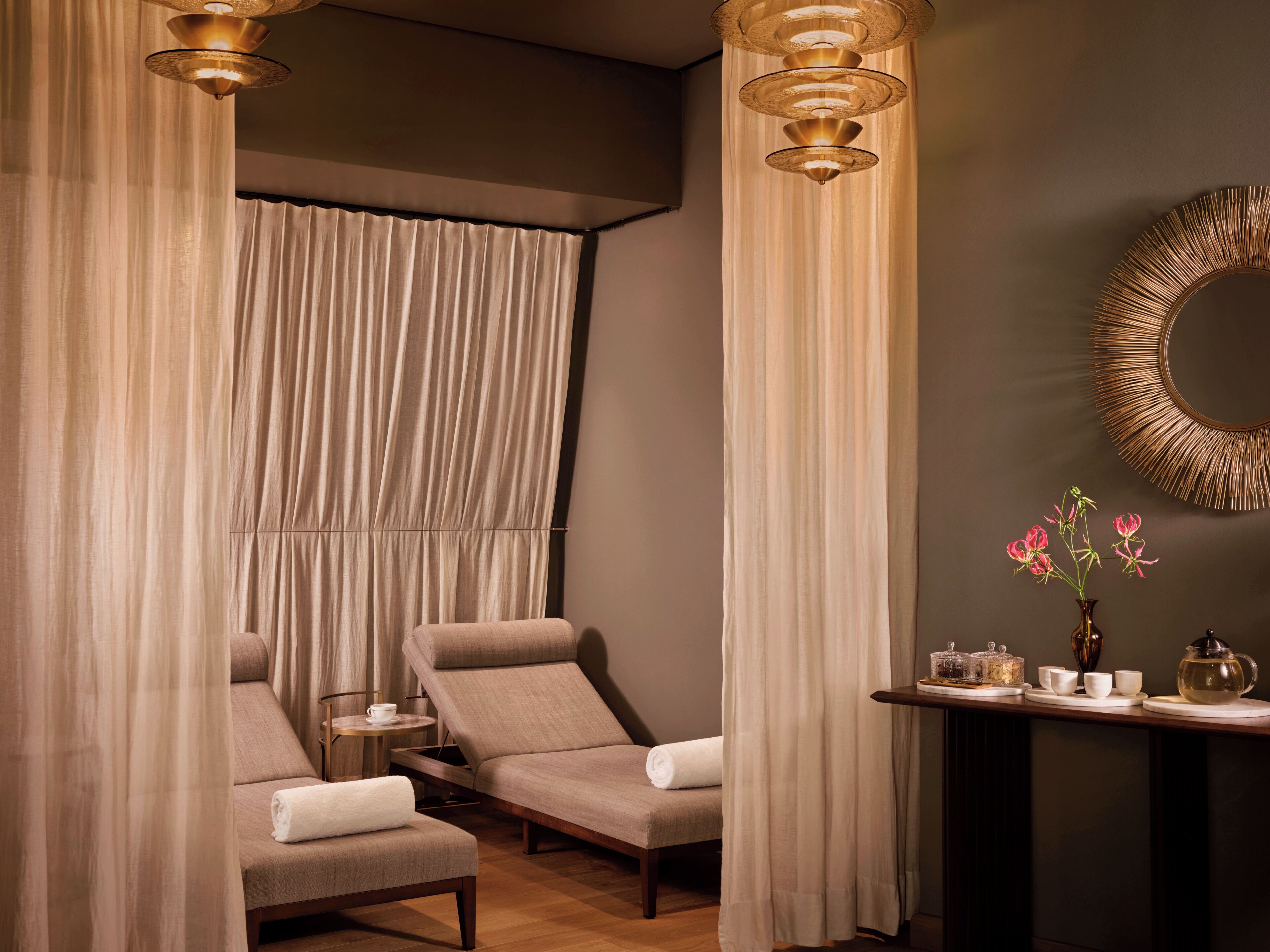 A spa room with two reclining chairs, a small table with a teapot, cups, and a vase with flowers.
