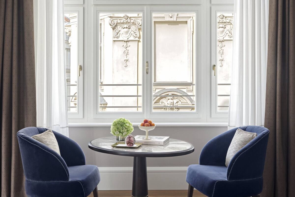 A room with a round table, two blue chairs, a vase with flowers, and a book.
