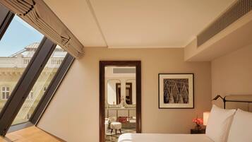 Una habitación de hotel con una cama grande, una obra de arte enmarcada, una mesita de noche y vistas a un edificio a través de una ventana.