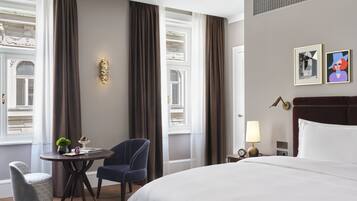 A hotel room with a large bed, a round table with two chairs, a small side table with a lamp, and two framed pictures on the wall.