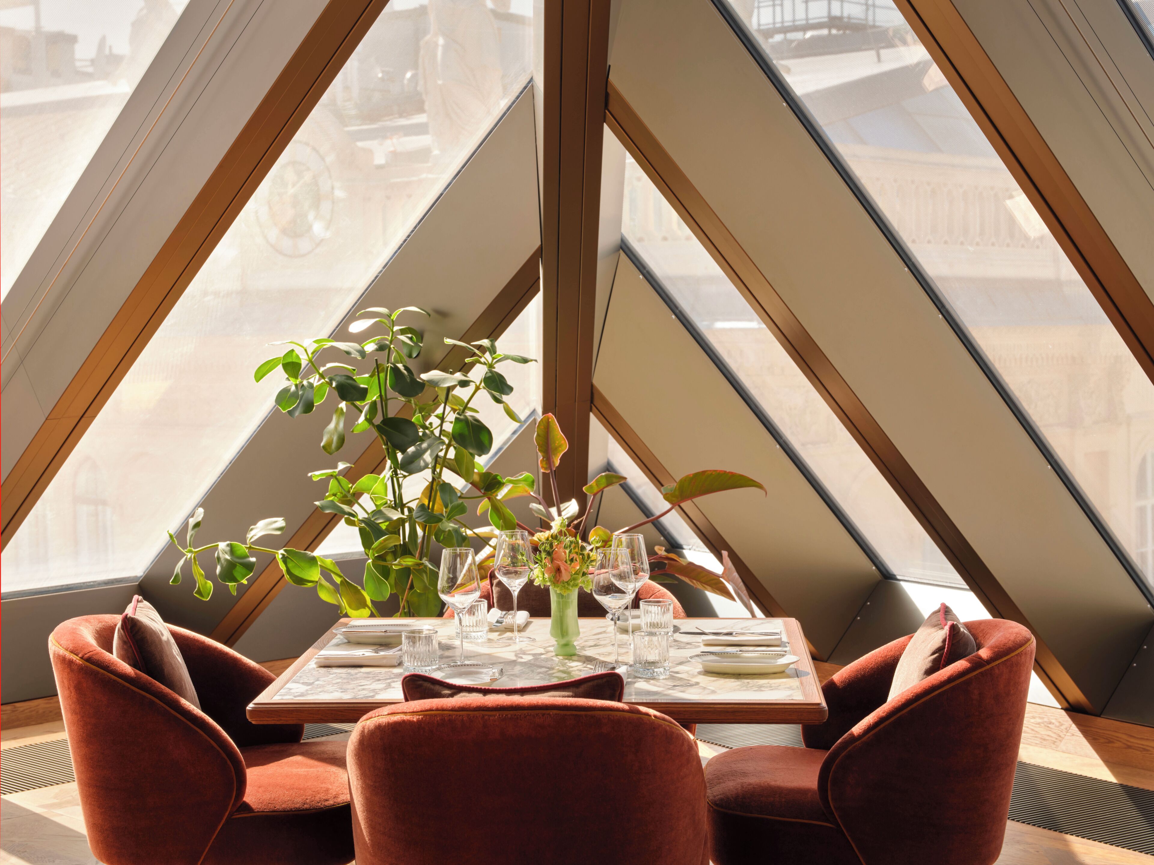 Un comedor con una mesa dispuesta para dos, una planta en maceta y vistas a través de amplios ventanales.
