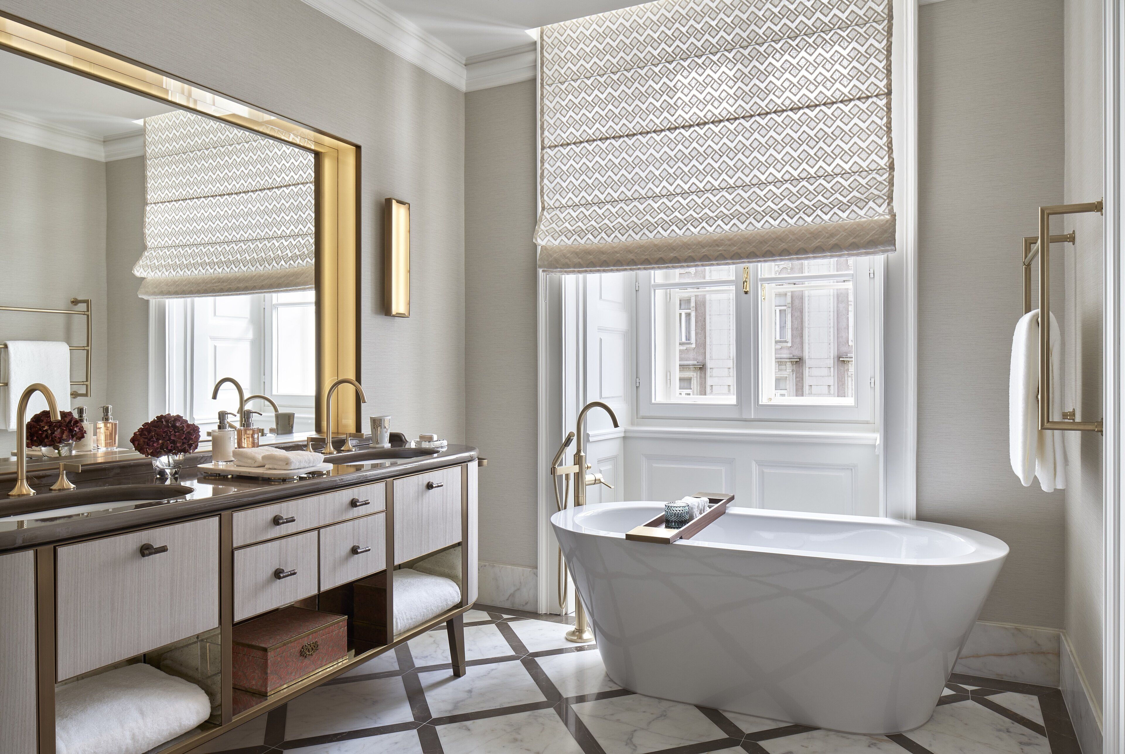 Une salle de bain moderne avec une baignoire sur pieds, un grand miroir et une fenêtre avec des stores à motifs.