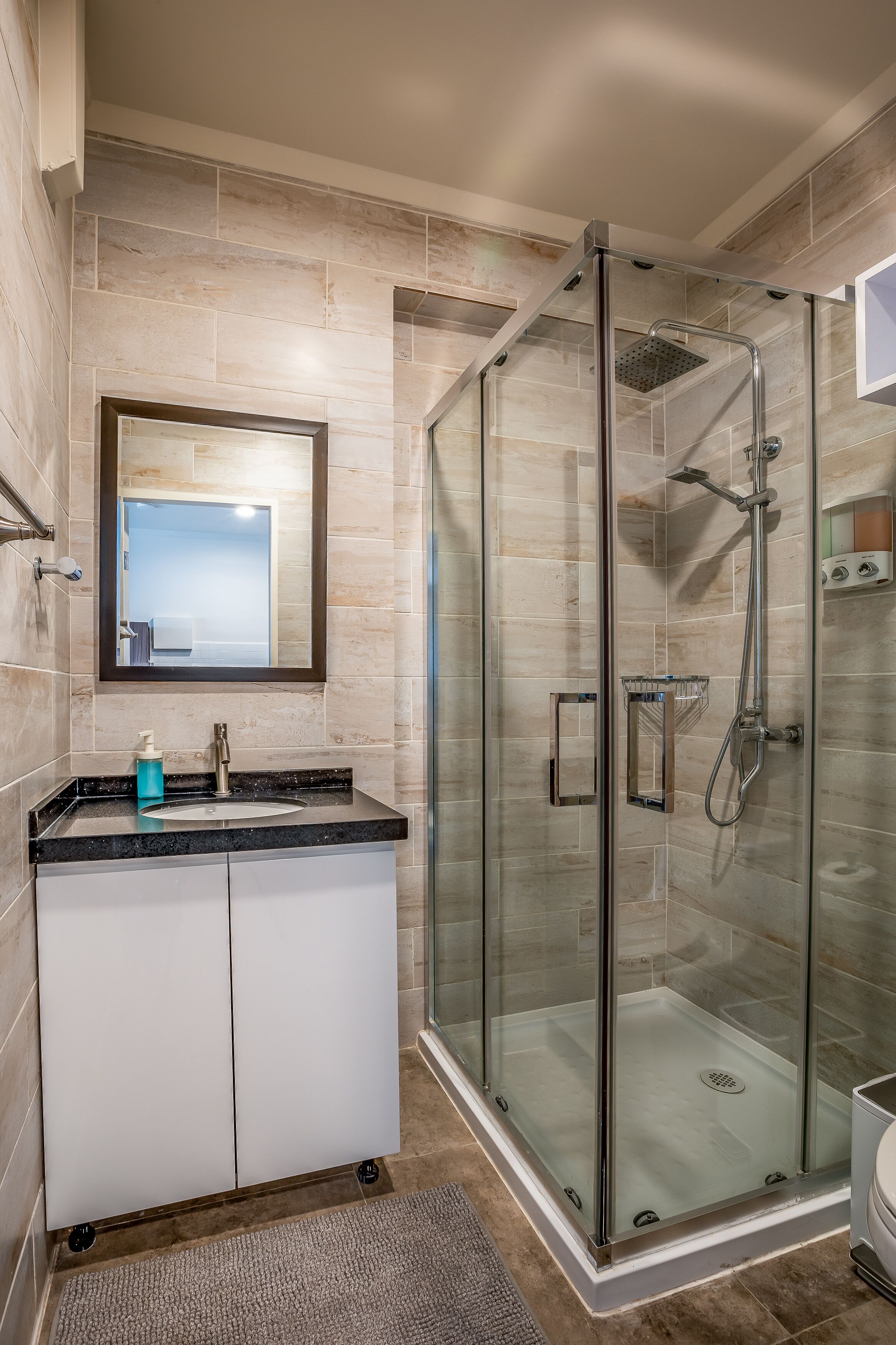 A modern bathroom with a glass-enclosed shower, a sink with a marble countertop, and a large mirror above the vanity.