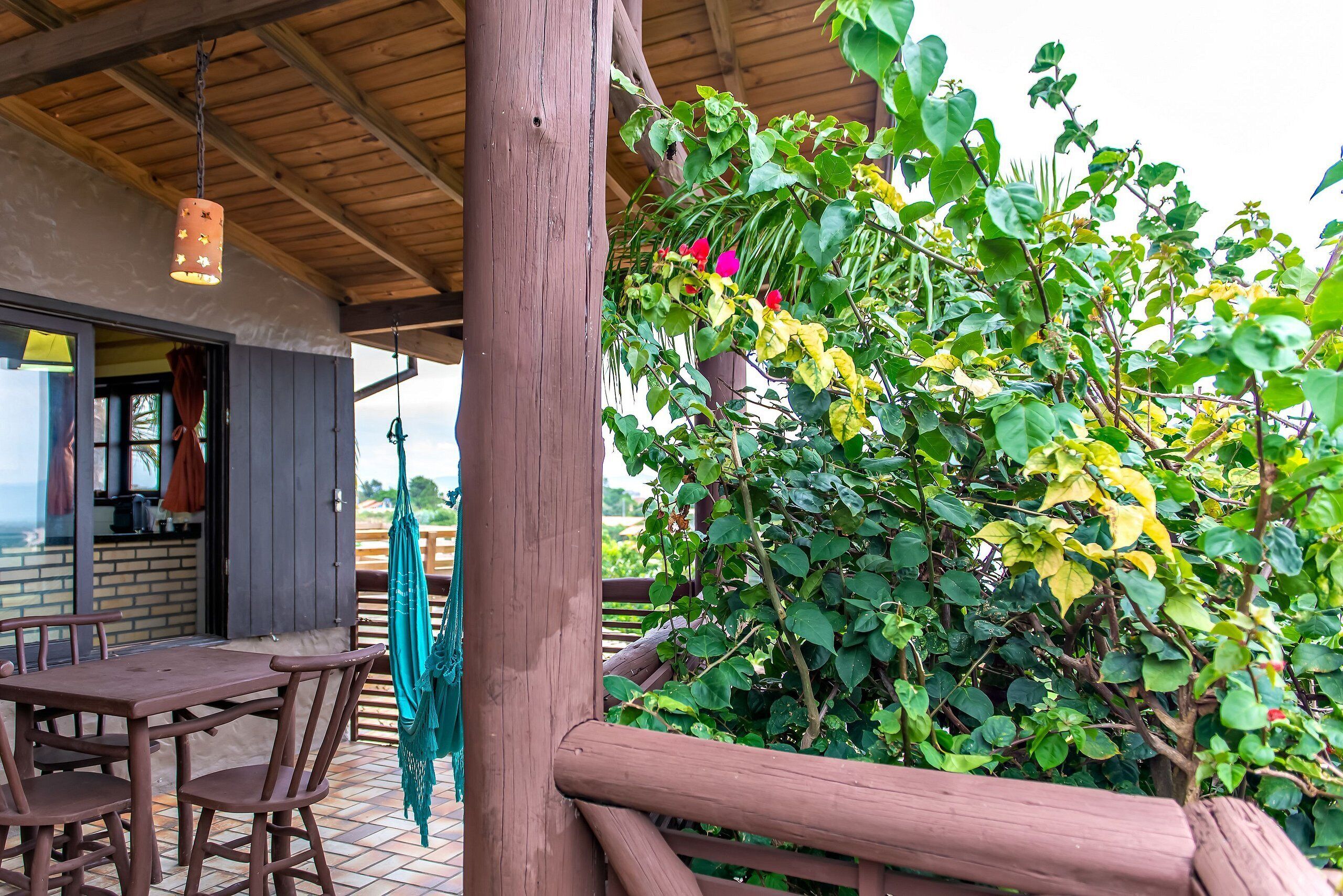 A wooden deck with a table and chairs, surrounded by lush greenery and a hanging light fixture.