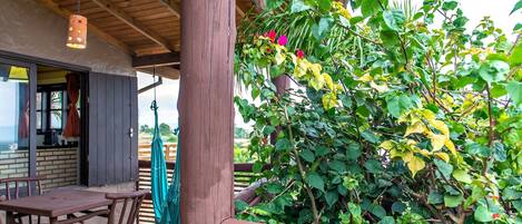 A wooden deck with a table and chairs, surrounded by lush greenery and a hanging light fixture.