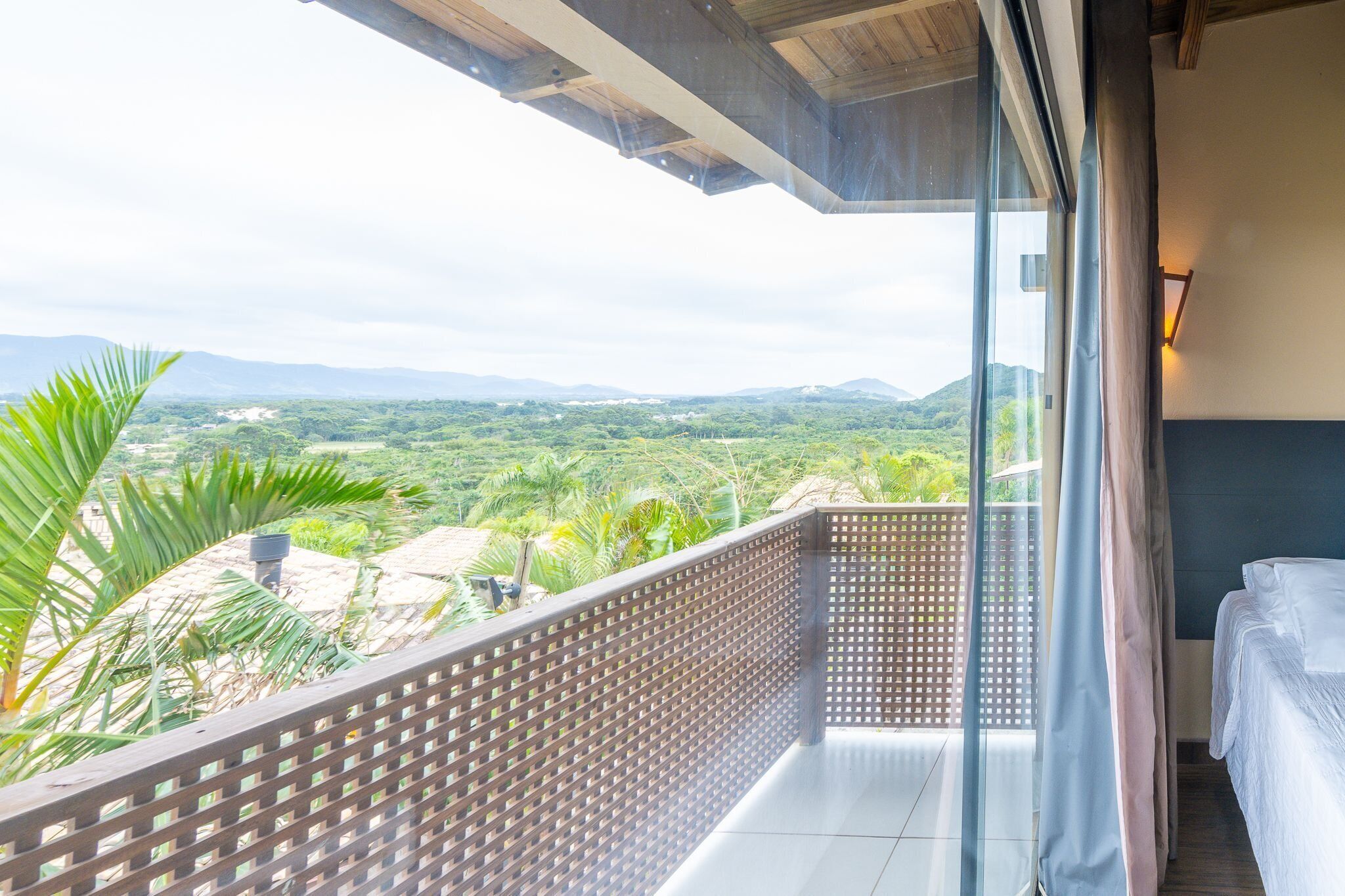 Un balcón con vistas a un paisaje exuberante, una cama y un techo de madera.