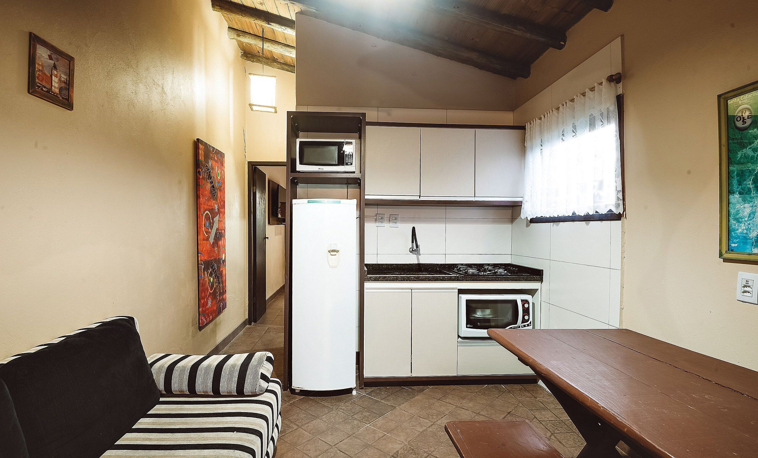 A compact kitchen with a refrigerator, microwave, stove, and oven. There is a wooden bench and a striped sofa.