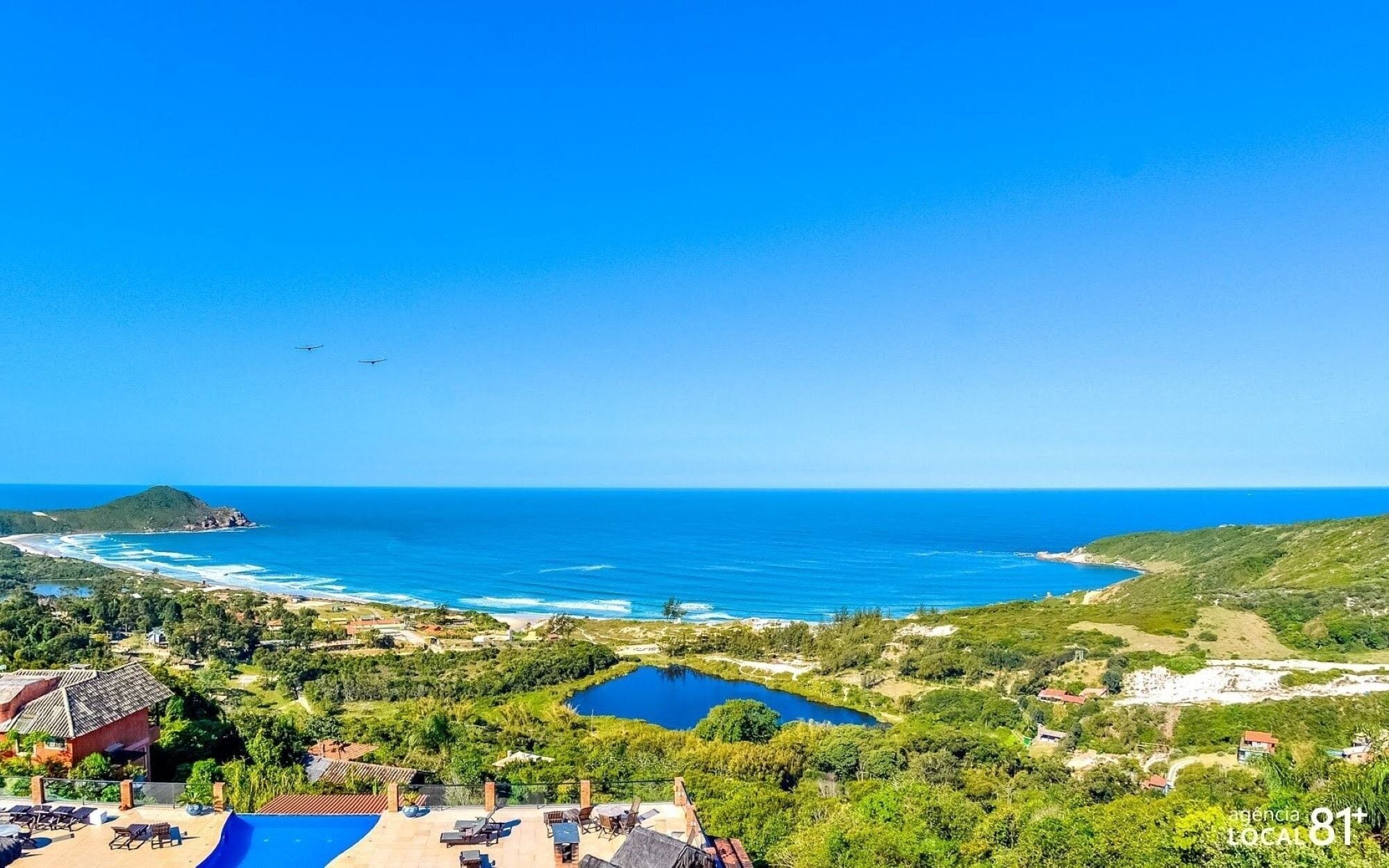 A coastal landscape with a swimming pool, lounge chairs, and a view of the ocean.