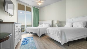 Ein Hotelzimmer mit zwei Betten, einem Schreibtisch, einem Sessel und einem Deckenventilator, mit Blick ins Freie.