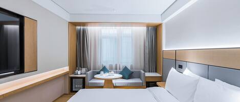 A modern hotel room with a large bed, a seating area with a table, and a TV.