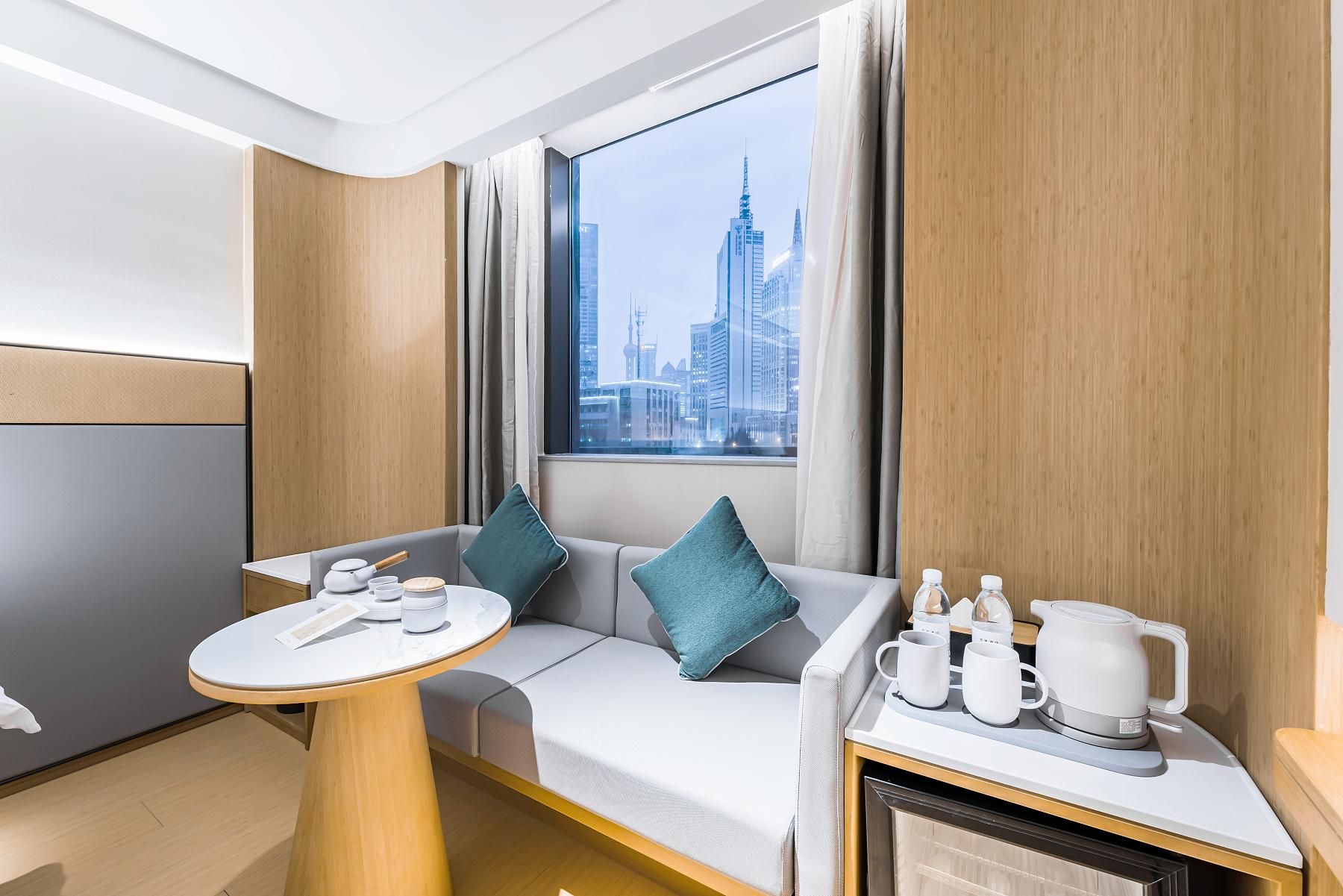 Ett modernt hotellrum med utsikt över staden, en soffa, ett litet bord och en liten köksdel.