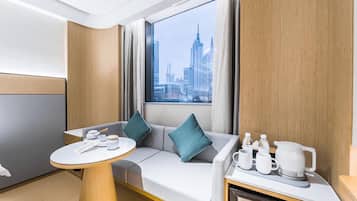 Habitación de hotel moderna con vista a la ciudad, un sofá, una mesita y un espacio con kitchenette.