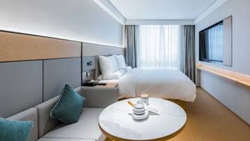 Una habitación de hotel moderna con cama, sofá, una mesita y televisor.