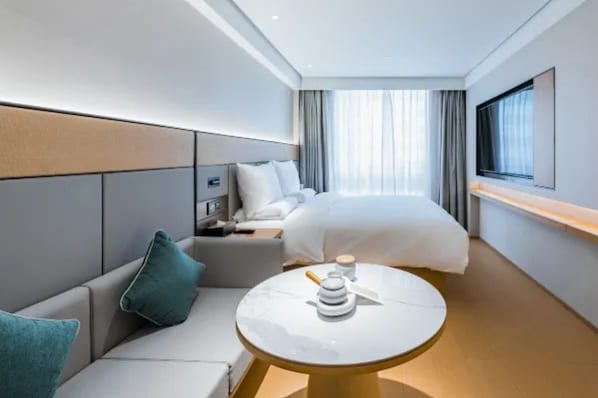 A modern hotel room with a bed, a sofa, a small table, and a TV. - Ji Hotel (Shanghai)