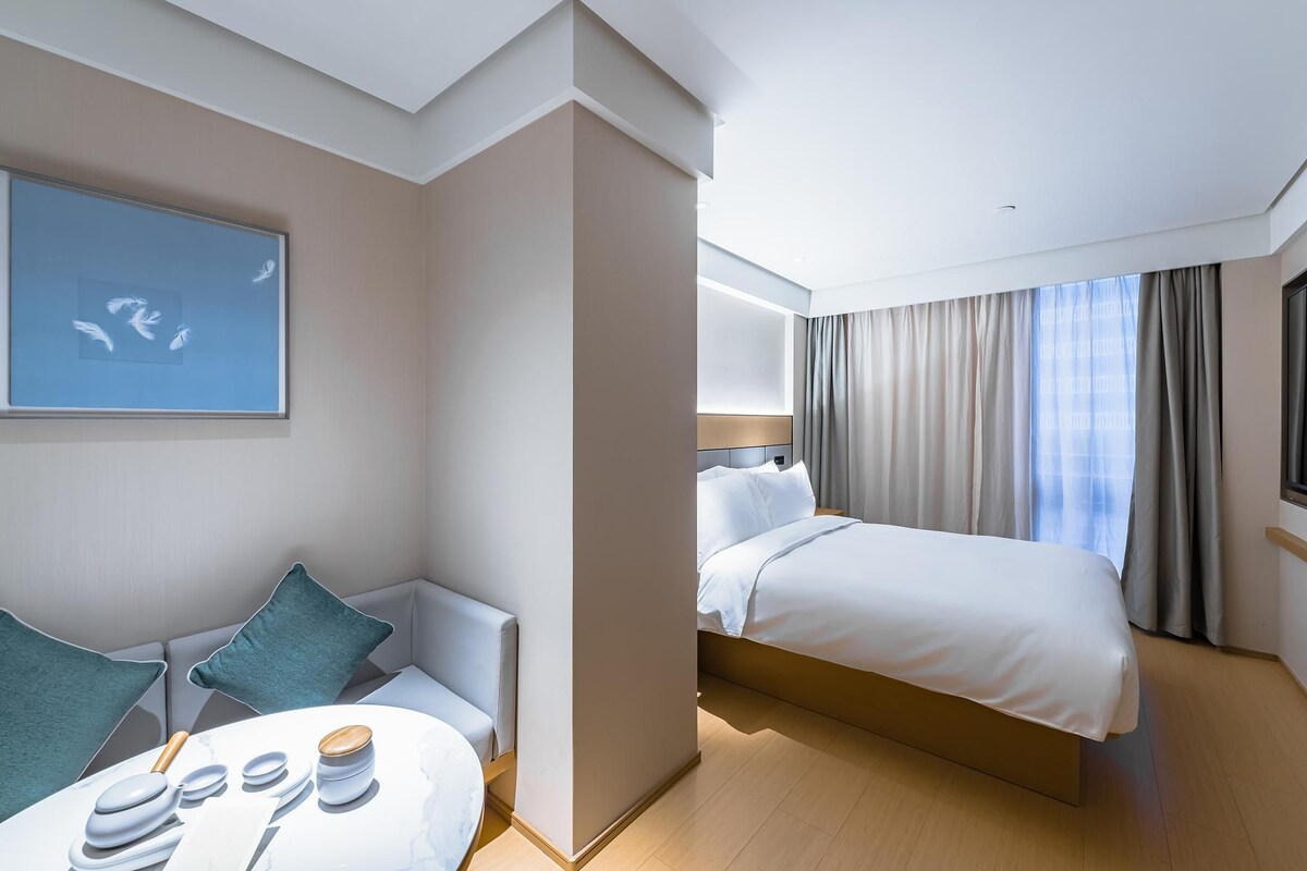A hotel room with a bed, a seating area with a table, and a painting on the wall.