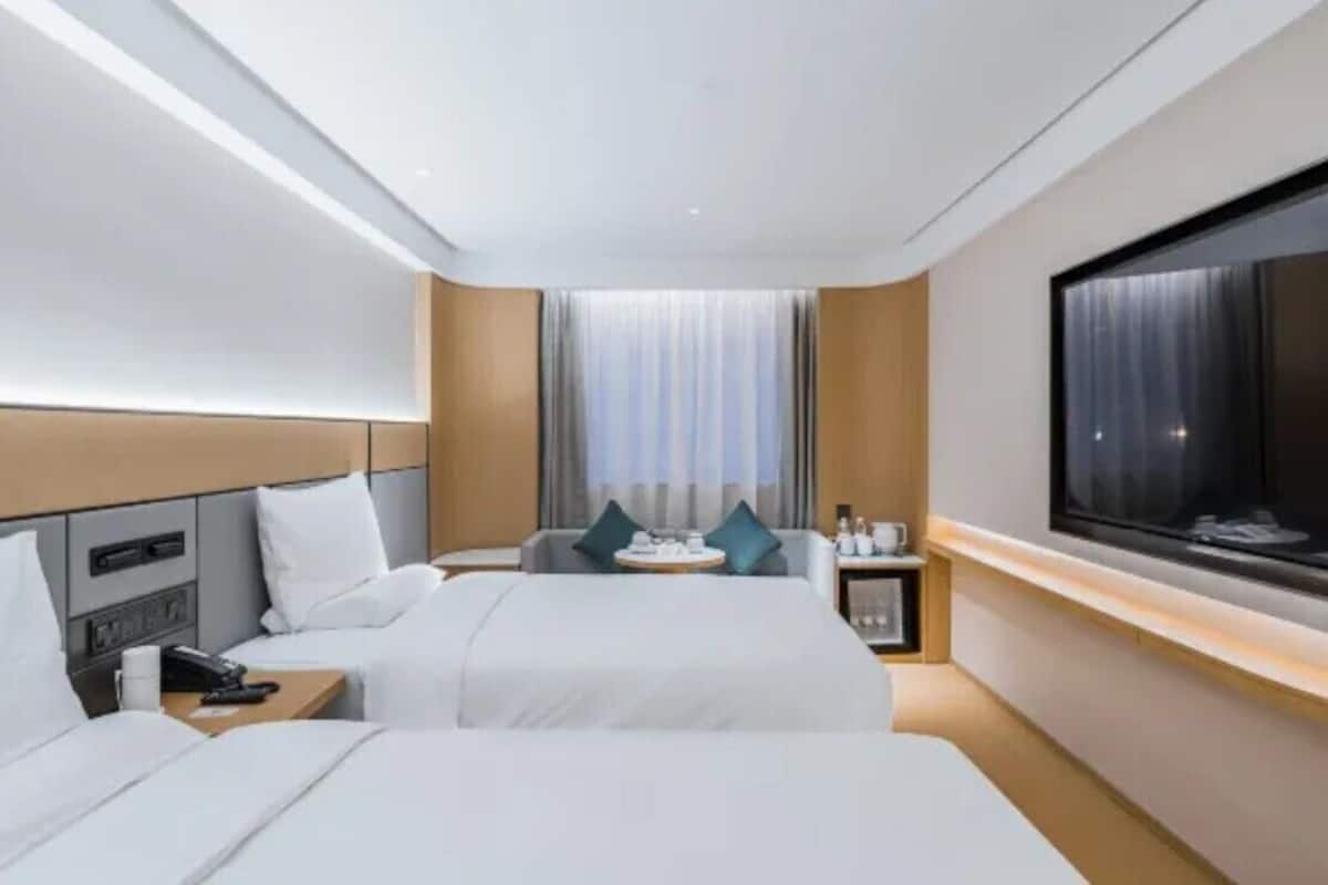Une chambre d’hôtel avec deux lits, une télévision, une table de chevet avec une lampe et une fenêtre avec des rideaux.