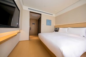 Una habitació d'hotel amb un llit, una televisió penjada a la paret i una porta que dona a un passadís.