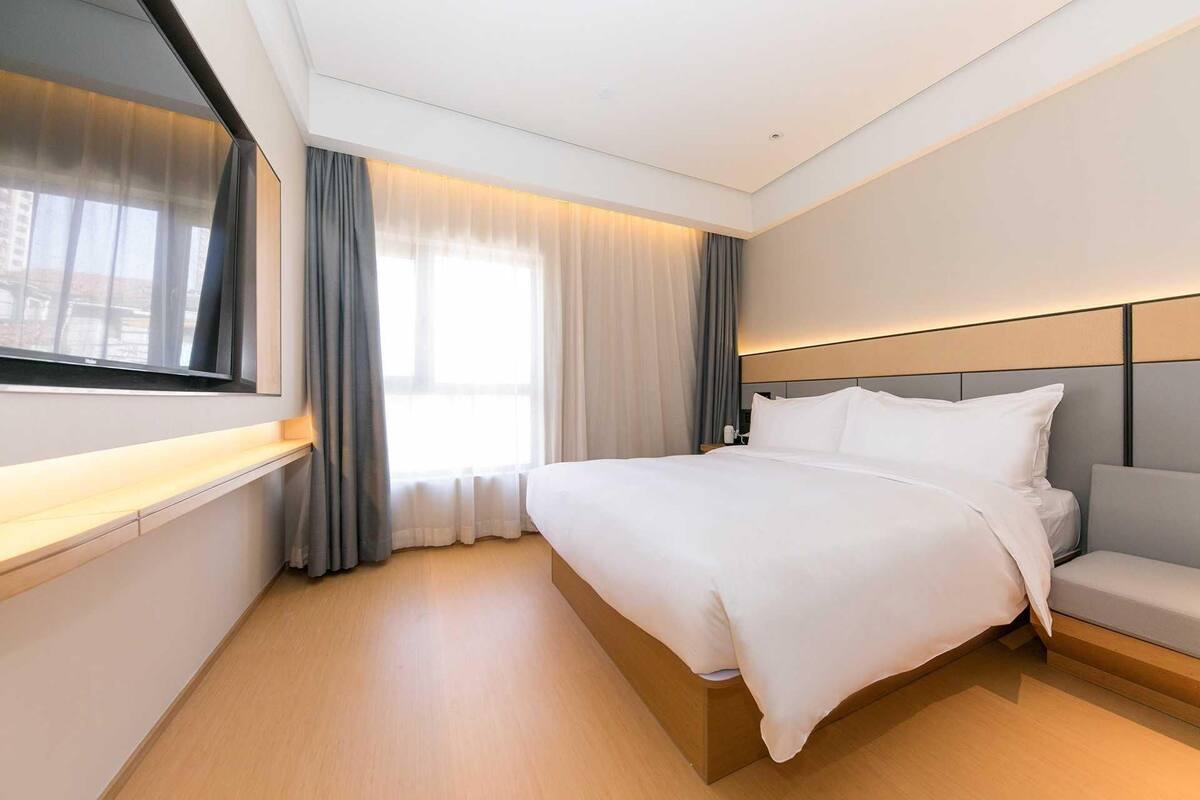 Une chambre d’hôtel moderne avec un grand lit, une table de chevet, une télévision et une fenêtre avec des rideaux.