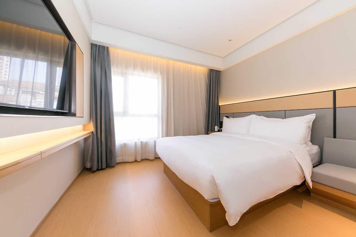 Una habitación de hotel moderna con una cama grande, una mesita de noche, un televisor y una ventana con cortinas.