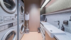 A laundry room with multiple Haier washing machines, a dryer, a vacuum cleaner, and a sink with a soap dispenser.