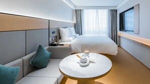 A modern hotel room with a bed, a sofa, a small table, and a TV.