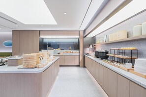 A modern kitchen with a central island, a view into the dining area, and a counter with various food items. - Ji Hotel (Shanghai)