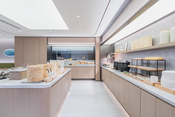 A modern kitchen with a central island, a view into the dining area, and a counter with various food items.