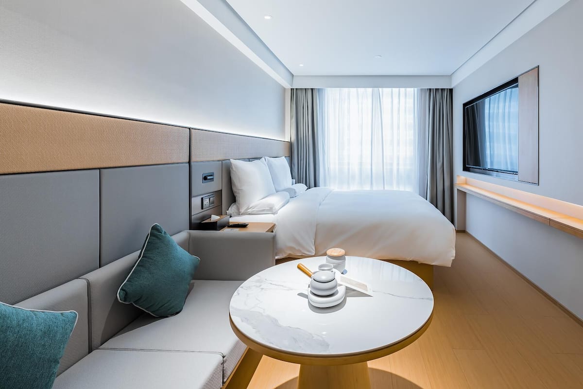 Una habitación de hotel moderna con una cama, un sofá, una mesita y un televisor.