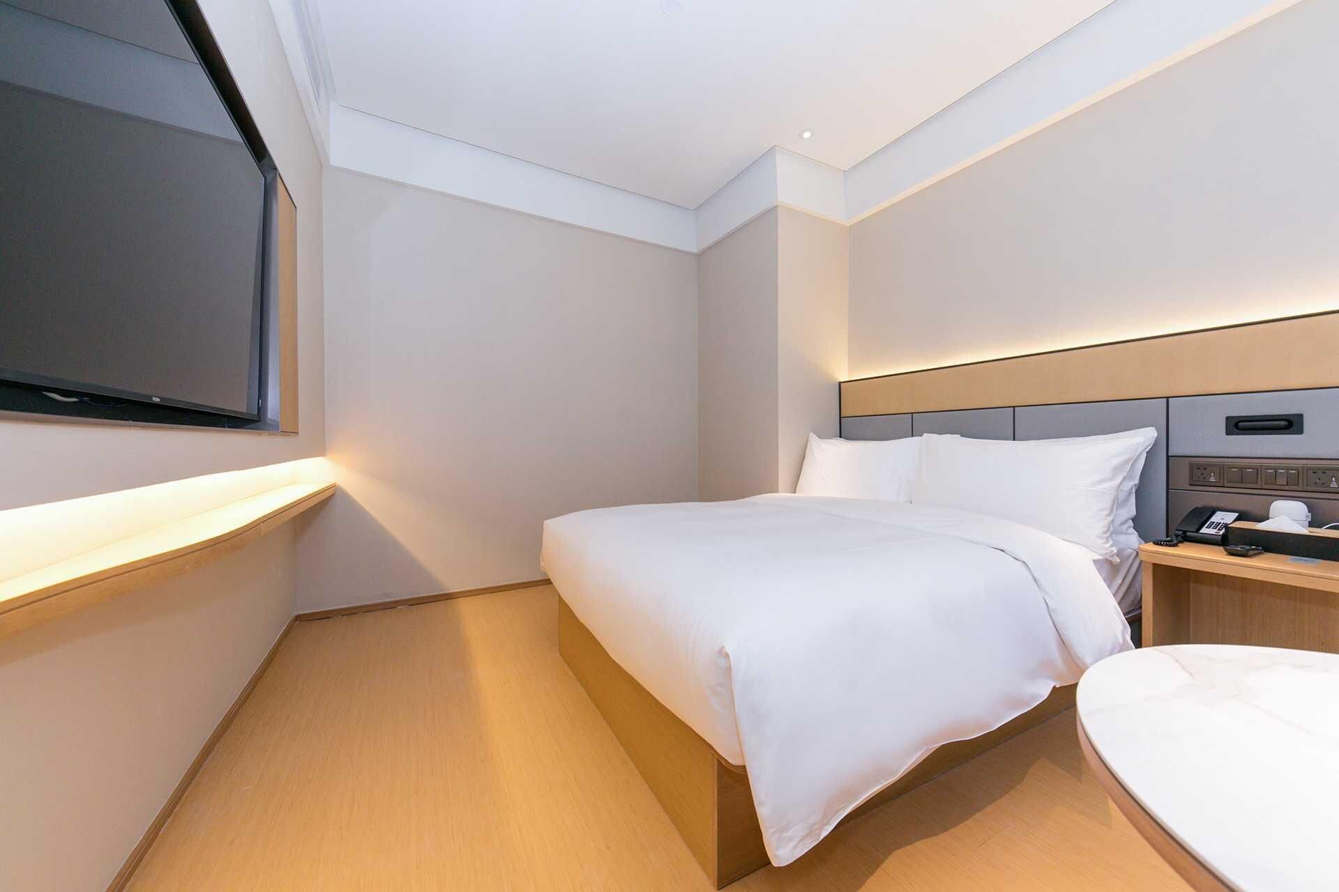 Una camera d'albergo con un letto, un comodino e una TV montata a parete.